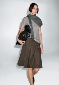 Gray short-sleeve t-shirt paired with a gray scarf, brown pleated skirt, and a black oversized clutch bag. Smooth textures and neutral colors.