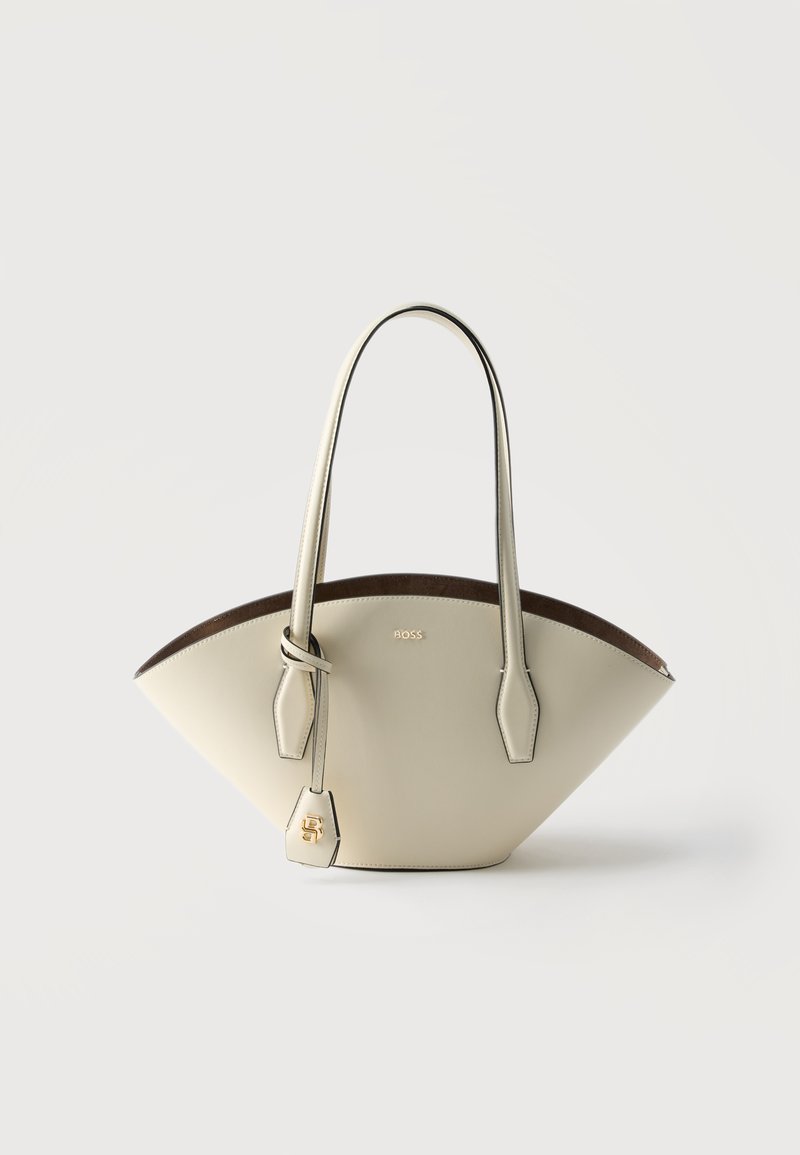 Τσάντα χειρός από δέρμα χρώματος κρέμας με ευρύ σχήμα τραπεζίου, διπλούς ιμάντες ώμου και χρυσή ετικέτα λογότυπου σε απλό φωτεινό φόντο.