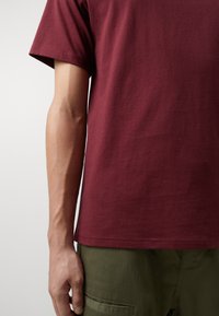 Camiseta de algodón burdeos con cuello redondo y mangas cortas, que presenta un corte relajado y una textura suave, combinada con pantalones verde oliva.