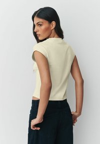 Világos sárga, magas nyakú és rövid ujjú testhez simuló póló, fekete, magas derekú nadrággal, oldalán zsebekkel párosítva.