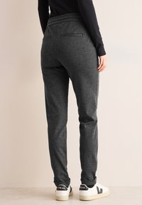 Jogging gris, fuselé, avec un tissu texturé, une ceinture élastique et des poches latérales, associé à des baskets blanches avec des accents noirs.