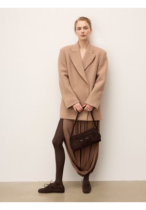 Manteau oversize en mélange de laine beige, robe drapée marron avec tissu froncé, collants marron et chaussures en daim marron foncé avec sac à main.