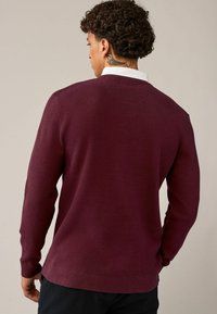 Pull en tricot bordeaux avec une finition texturée, à manches longues et au design en V. Poignets et ourlet côtelés avec un intérieur lisse.