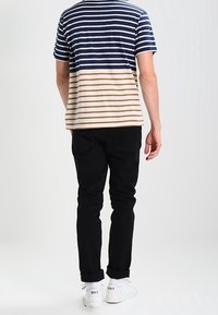 Pestrý pruhovaný tričko v námořnické modři a krémové barvě, spojené s černými džíny a bílými teniskami, z pohledu zezadu.