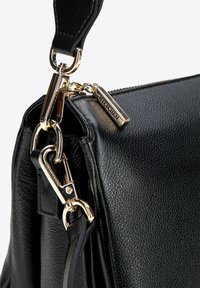 Czarna skórzana torebka o fakturowanej powierzchni, z elementami w złotym kolorze oraz zawieszką na suwaku z napisem "WITTCHEN". W zestawie odpinany pasek.