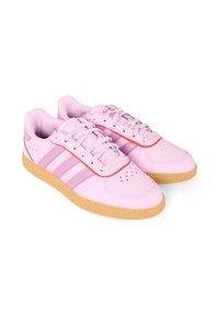 Różowe sneakersy wykonane z materiału syntetycznego, z sześcioma oczkami, trzema paskami z boku, gumową podeszwą i czerwonym akcentem na języku.