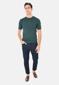 Top corto a maniche corte in maglia a coste verde scuro abbinato a pantaloni in denim scuro con cuciture a contrasto e scarpe in pelle marrone.