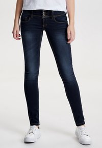 Mörkblå skinny jeans med femknappsknäppning, klassiska fickor och kontrasterande sömnadsdetaljer. Bärs med vita sneakers.