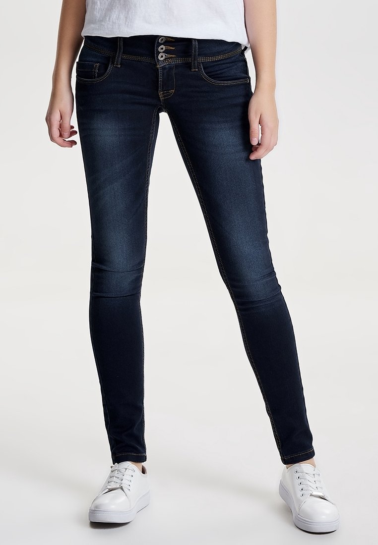Mörkblå skinny jeans med femknappsknäppning, klassiska fickor och kontrasterande sömnadsdetaljer. Bärs med vita sneakers.
