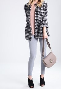 Manteau à motif pied-de-poule noir et blanc, haut rose clair, jean skinny gris, escarpins noirs à bout ouvert, et sac à main texturé taupe.