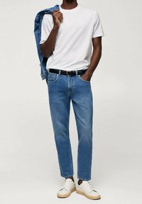 Camiseta blanca, jeans de mezclilla azul y zapatillas blancas. La chaqueta es de mezclilla azul claro. Estilo sencillo, corte relajado y diseño clásico.