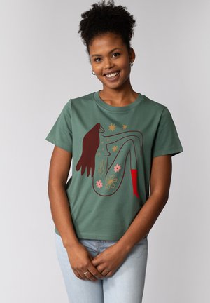 Groene katoenen T-shirt met een grafisch ontwerp van een figuur met rode accenten, omringd door bloempatronen en sterren. Korte mouwen, relaxte pasvorm.