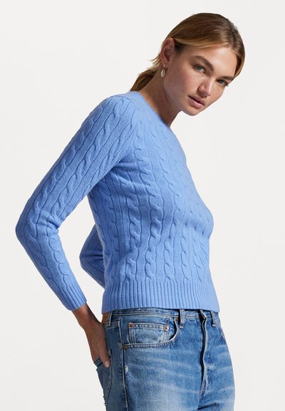 Šviesiai mėlynas megztinis su kabliukais, ilgomis rankovėmis, guminate apatine dalimi ir prigludusia siluetu, derinamas su suplyšusiomis džinsinėmis kelnėmis.