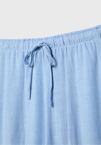 Tissu bleu clair, texturé, avec une taille élastique et un système de fermeture à cordon. Accent sur le design simple et décontracté du vêtement.