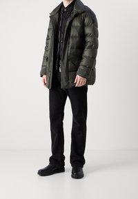 Chaqueta de abrigo verde con cuello alto y bolsillos con cremallera, combinada con jeans negros y botas negras. Textura suave y brillante, corte casual.