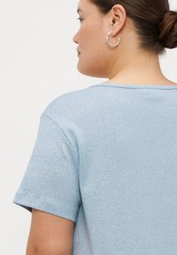 T-shirt metálico azul claro com mangas curtas, decote redondo e uma textura suave, apresentando um ligeiro brilho.