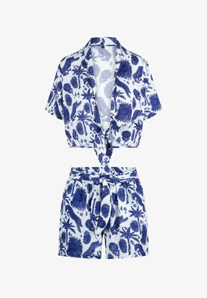 Kortærmet crop top med knapper foran og højtaljede shorts sæt med blå dyre- og blomsterprint på hvidt stof, med bindedetaljer foran.