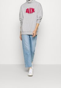 Felpa grigia oversize con logo rosso "AIX", polsini e orlo a coste. Abbinata a jeans blue chiaro a gamba dritta e sneakers bianche.