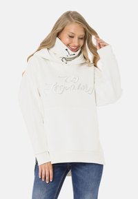 White hooded sweatshirt with "Legendary" in metallic thread, soft fabric, kangaroo pocket, and drawstring neck. Paired with blue jeans.