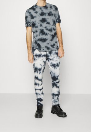 Heren tie-dye outfit bestaande uit een grijs-zwart T-shirt met korte mouwen en bijpassende grijs-witte sweatpants, gecombineerd met zwarte veterlaarzen.