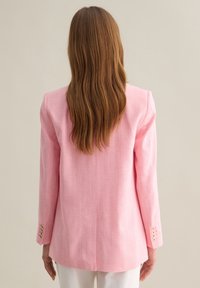 Blazer rosa con righe bianche verticali, design su misura, maniche lunghe e polsini abbottonati. Tessuto strutturato, stile minimalista.
