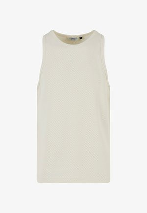 Białe siatkowe top bez rękawów w połączeniu z oliwkowymi szerokimi spodniami. Model stoi z rękami w kieszeniach, nosząc białe i szare sneakersy.