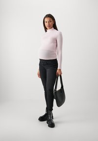 Maglione aderente rosa chiaro con collo alto, jeans skinny neri e stivali neri alla caviglia chunky, abbinati a una borsa a spalla nera.
