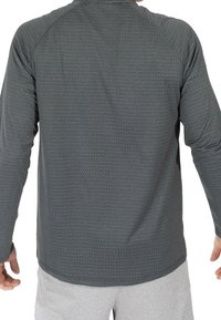 Langärmliges, dunkelgraues Sportshirt mit strukturiertem Muster und Raglansleeves. Der Stoff ist glatt und flexibel, ideal für Sportbekleidung.