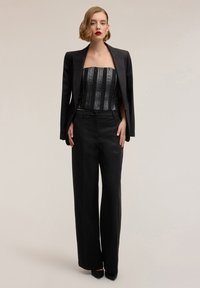 Blazer in satin nero sopra un top senza spalline decorato con paillettes e righe verticali, abbinato a pantaloni neri a vita alta e gambe ampie.