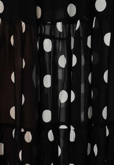 Μαύρο και διαφανές υφασμάτινο υλικό με μεγάλα λευκά πουά. Η σχεδίαση διαθέτει στρώσεις με βολάν και έναν συνδυασμό αδιαφανών και διαφανών τμημάτων.