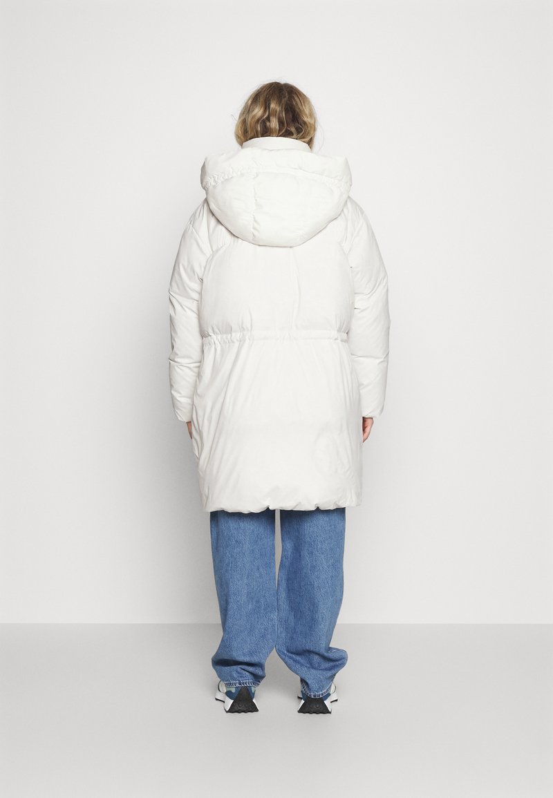 Chaqueta de plumas blanca con capucha, cubierta con una tela suave y brillante. Presenta una cintura elástica, diseño hasta las rodillas y un ajuste oversize.