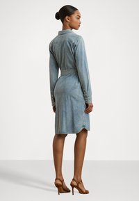 Denim shirt dress in faded blue, featuring a structured collar, long sleeves, a belted waist, and a curved hemline.