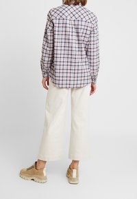 Långärmad rutskjorta i ljusrosa och marinblå, i bomullsblandning, med rundad nederkant. I kombination med vida krämfärgade byxor och beige sneakers.