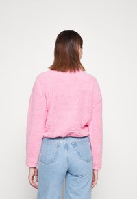Maglione cropped fuzzy rosa con tessuto testurizzato, colletto a giro, e spalle scese, abbinato a jeans chiari a vita alta.