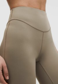 High-waisted leggings in a light beige color, made of stretchy fabric with flat seams and a smooth texture, featuring a simple design.