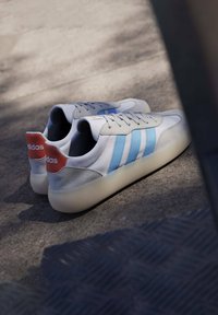 Vita sneakers med ljusblå ränder, grå accenter och orange hälflik. Slät läderöverdel med en texturerad mockafinish och gummisula.