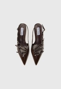 Tacchi slingback in pelle lucida marrone con punte appuntite e tre fibbie decorative. Texture liscia, design minimalista.