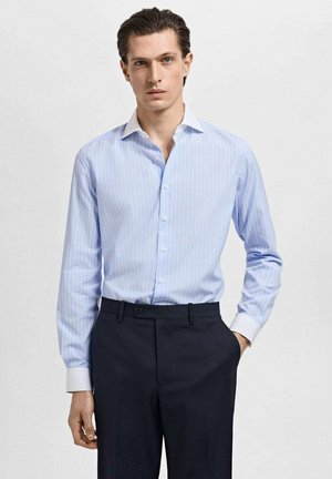 Light blue striped dress shirt with a white collar, long sleeves, and button-up front, worn with dark tailored trousers. Smooth fabric.