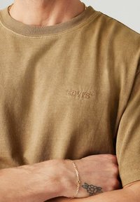 Kurzärmliges, olivgrünes Baumwoll-T-Shirt mit geripptem Kragen und dezentem, gesticktem "Levi's"-Logo auf der Brust. Angenehme Textur.