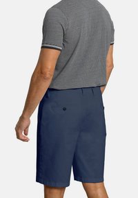 Pantalones cortos navy fabricados con tejido ligero, con bolsillos traseros con cierre de botón y un diseño de frente plano. Camisa polo texturizada encima.