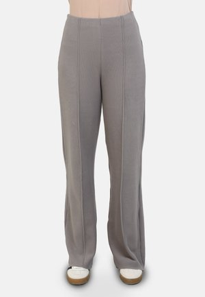 Pantaloni grigi chiari, a gamba larga, realizzati in tessuto morbido con cuciture verticali e vita alta. Indossati con sneaker bianche.