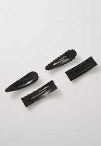 Sorte plastik hårnåle med bølgede kanter og flere sprækker for greb, arrangeret diagonalt på en lys baggrund.