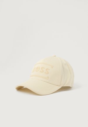 Kremna baseball kapa iz teksturiranega blaga, z reljefnim logotipom "BOSS" spredaj in ukrivljenim robom.