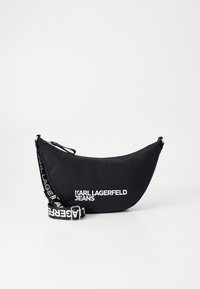 Borsa a spalla nera in nylon con forma curvata. Presenta un logo bianco prominente, chiusura con zip e una tracolla con un motivo a logo ripetuto.