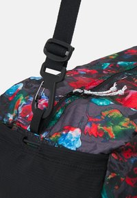 Mustat kukkakuosiset duffel-tyyliset laukut, joissa on monivärisiä kuvioita, varustettu vetoketjulla ja klipsikiinnityksellä. Teksturoitu kangas ja kestävä hihna.