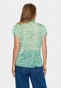Blusa verde trasparente con motivo a stampa leopardata, caratterizzata da maniche a puff corte e una morbida sfumatura. Realizzata in tessuto leggero e fluente.