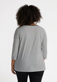 Svart och vit randig långärmad topp med rund halsringning och avslappnad passform, tillsammans med svarta byxor. Slät tyg och avslappnad design.