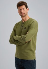 Olijfgroen lange mouwen henley shirt met een kraag met drie knopen, gestructureerde stof, zijsplitten en een klein merklabel op de borst.
