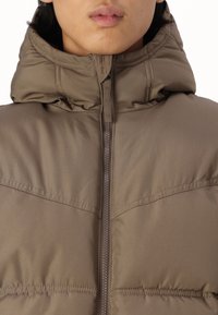 Brown puffer jacket with a high collar and zip closure. Features stitched accents and a smooth, matte texture.