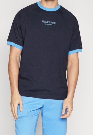 Mand iført navyblå T-shirt med lyseblå krave og ærmekanter, "Hilfiger New York" tekst på brystet, kombineret med lyseblå shorts.